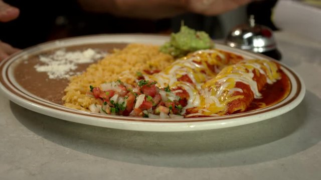 Close up shot of a tasty enchilada platter being placed on the counter and picked up by a server at a family owned Mexican restaurant