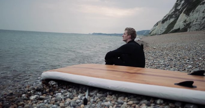 Paddle boarder sitting by sea looking out