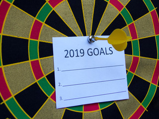 Concept of achieving a goal. Dart game with dart on paper that write: 2019 GOALS words for goals...
