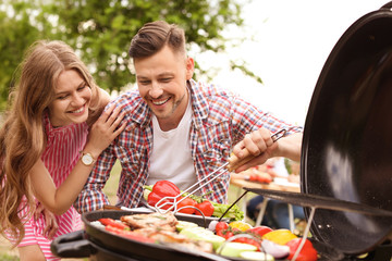 Young couple having barbecue with modern grill outdoors