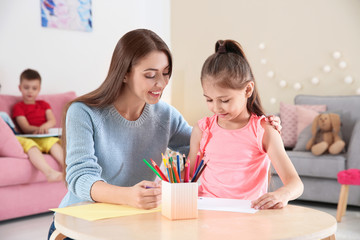 Cute little child drawing at table with young woman in playing room