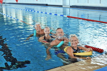 Naklejka premium Sportive senior people doing exercises in indoor swimming pool