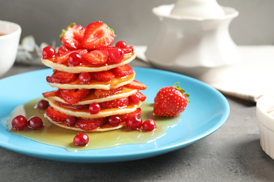 Tasty pancakes with berries and honey on plate