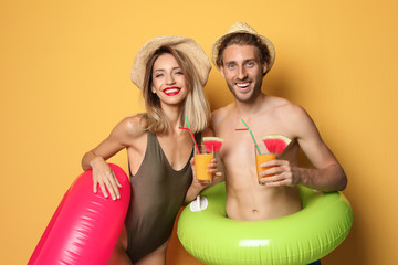 Fototapeta premium Happy young couple in beachwear with inflatable rings and cocktails on color background