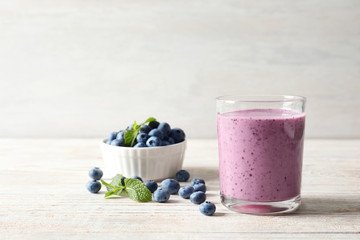 Tasty blueberry smoothie in glass, bowl with berries on table against light background with space for text