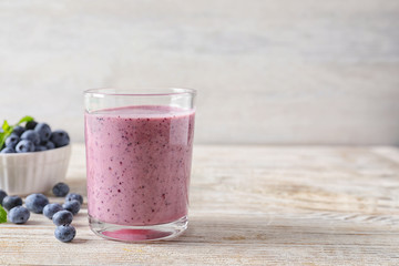 Tasty blueberry smoothie in glass, bowl with berries on table against light background with space...