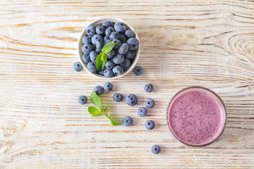 Tasty blueberry smoothie in glass and bowl with fresh berries on wooden table, top view