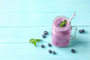 Tasty blueberry smoothie in mason jar, berries and space for text on wooden table