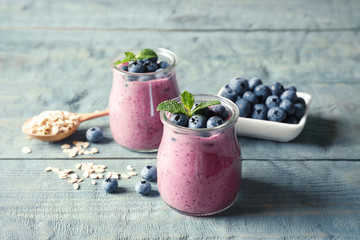 Tasty blueberry smoothie in jars, berries and oatmeal on wooden table