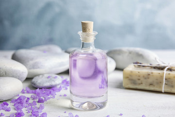 Bottle with natural herbal oil, soap and lavender flowers on table against blurred background