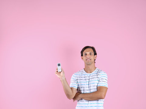 Young man with air conditioner remote on color background, copy space text