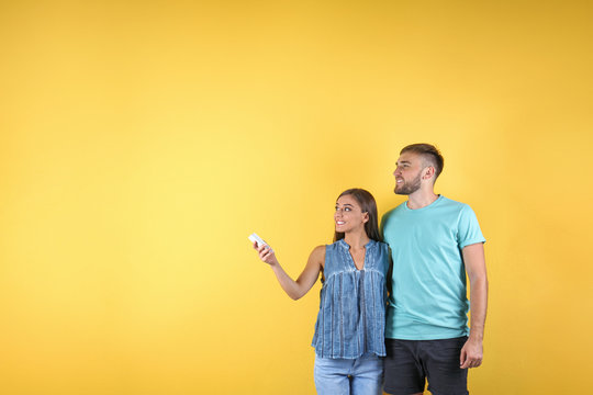Young couple with air conditioner remote on color background, copy space text
