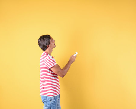 Young man with air conditioner remote on color background, copy space text