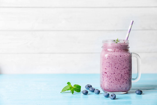 Tasty blueberry smoothie in mason jar on table against light background with space for text