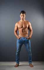 Shirtless young man in stylish jeans near grey wall