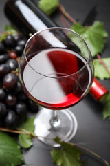 Glass and bottle of red wine and fresh ripe juicy grapes on table