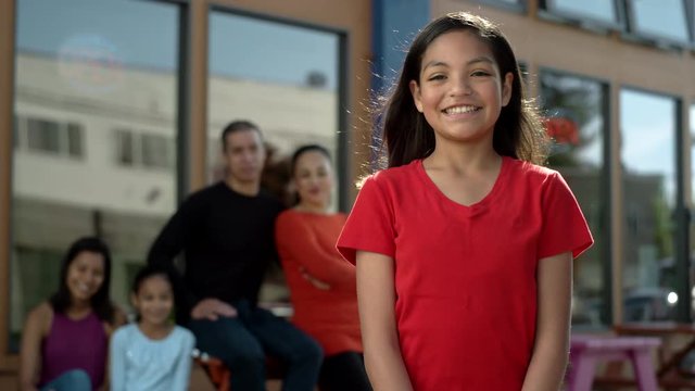 Portrait of a cute preteen girl of hispanic descent, with her family out of focus in the background, rolls her eyes and smiles in front of their family business