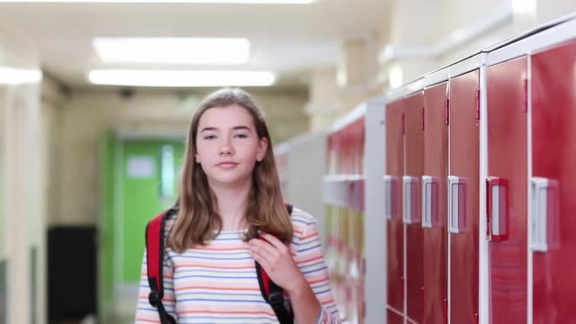 Portrait Of Female High School Student Walking Down Corridor And Smiling At Camera
