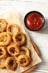 Homemade crunchy fried onion rings with tomato sauce on wooden table, top view
