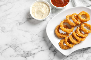 Homemade crunchy fried onion rings with sauces on marble table, top view. Space for text