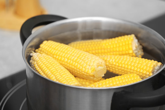 Stewpot with water and corn cobs on stove, closeup