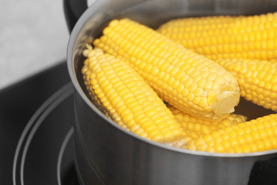 Stewpot with water and corn cobs on stove, closeup