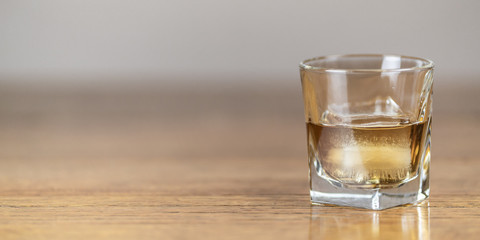 Whiskey in an elegant glass on the rocks with a large ice cube on a rustic wood table.