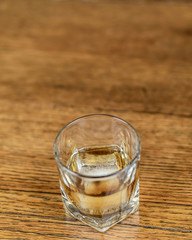 Whiskey in an elegant glass on the rocks with a large ice cube on a rustic wood table.