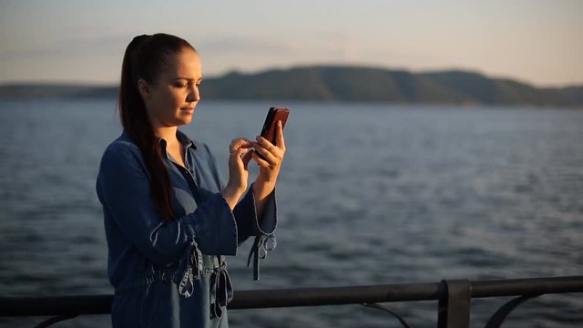 young beautiful Caucasian woman with red hair in the evening at sunset walking along the promenade and talking on the phone.