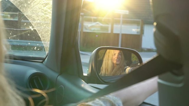 A young woman enjoys traveling in a car with an open window in the rays of the sunset and reflection in the rearview mirror. Slow motion.