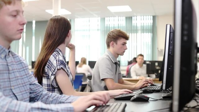 Teacher Helping Female High School Student Working In Computer Class