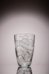 Glass of ice cubes grey background