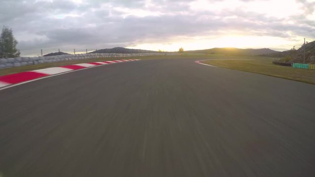 POV: Racing a car down the empty asphalt circuit on a beautiful golden evening. Cool first person view of racing a fast on a scenic racetrack at sunset. Picturesque landscape and the morning sky.