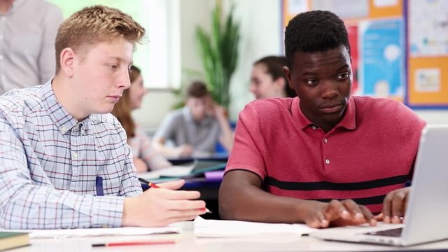 Teacher With Two Male High School Students Working At Laptop In Classroom