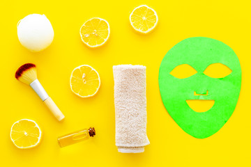 Face spa products. Facial mask, cream, oil near lemon slices and towel on yellow background top view