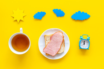 Parts of day. Morning. Time for breakfast. Tea, sandwich near alarm clock, sun and clouds cutout on yellow background top view