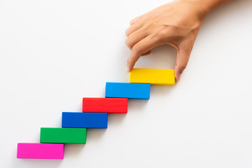 Concept of building success foundation. Women hand put red wooden block on colorful wooden blocks in the shape of a staircase.
