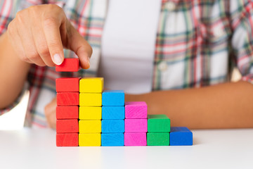 Concept of building success foundation. Women hand put colorful wooden blocks in the shape of a staircase