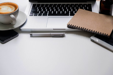 Office supplies are tablet, pen, computer, notebook, mobile phone and red coffee mug placed at an office desk and have a white background.