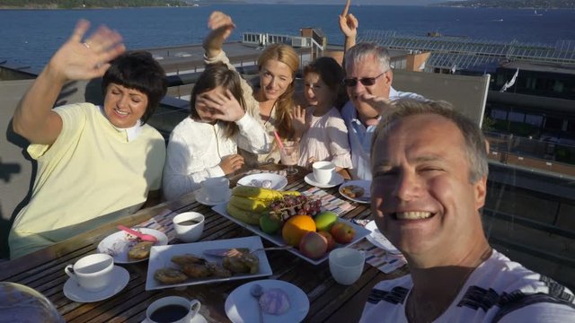 Big happy family takes a selfie or Uses Phone Video Call Camera sitting on the open terrace on the roof of the house on the sea coast.