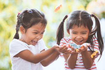 Two asian child girls having fun to catching candies falling from the sky and share to each other