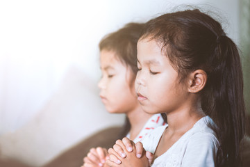 Cute asian child girl and her sister praying with folded her hand in the room together for faith,spirituality and religion concept