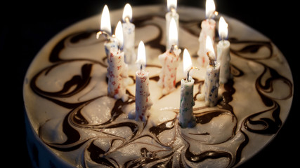 Birthday cake with colorful burning candles in dark.