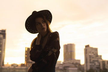 Beautiful girl posing at sunset in a dress and a round hat in the city