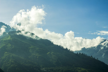 green mountain with snow peaks in the clouds