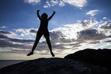 Woman jumping on cliffs in sunset