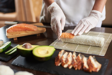 Closeup viev of chef hands preparing japanese food. Chef making sushi rolls at restaurant with many ingredients on the black stone plates.