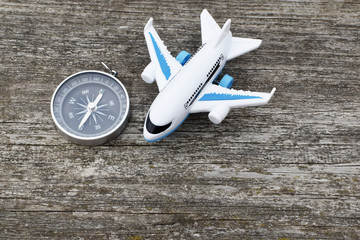 Air plane toy and traveler compass showing north on dark grey old weathered wooden surface background closeup view with copy space for text.  Travel planning and vacation trip concept. 