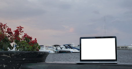 computer laptop with blank white screen on wooden table with yacht boats floating on the sea at background