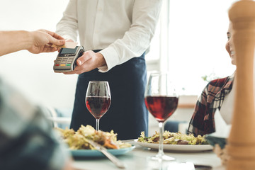 Payment with card. Nice professional waiter holding a money terminal while taking a payment